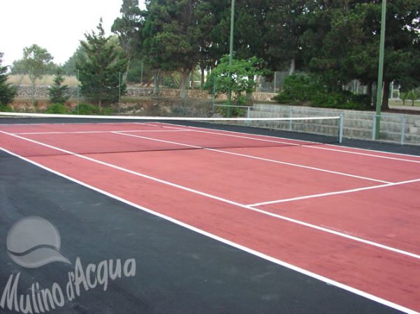 Campo da tennis con superficie rossastra e rete centrale.