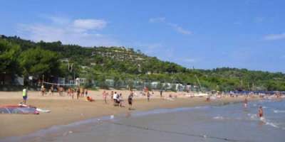 Spiaggia affollata con gente che gioca e colline verdi sullo sfondo.