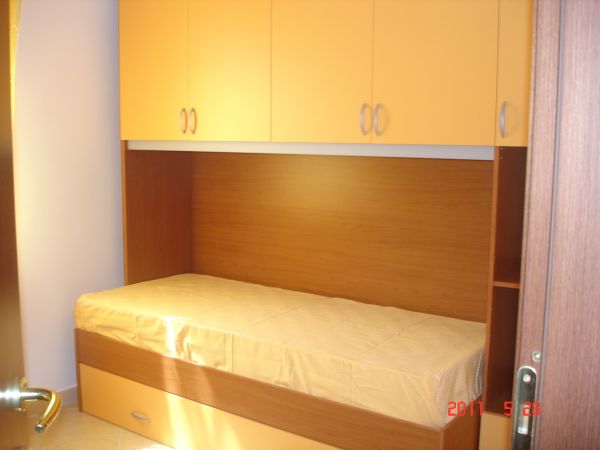 Letto singolo con armadi arancioni sopra.