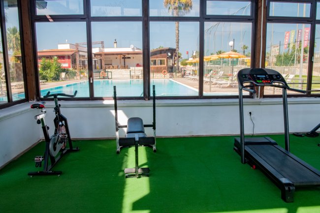 Palestra con cyclette, panca e tapis roulant, vista su piscina.