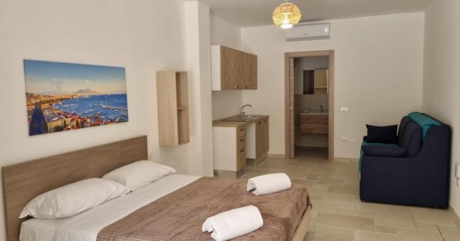 Camera moderna con letto, divano blu e cucina.