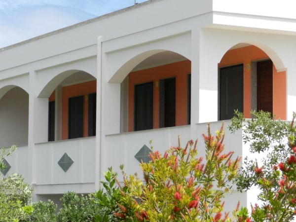 Facciata di edificio bianco con archi e cespugli fioriti.