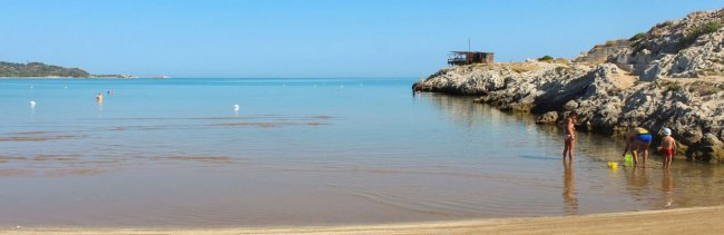 Spiaggia con sabbia e mare calmo, persone giocano in acqua.