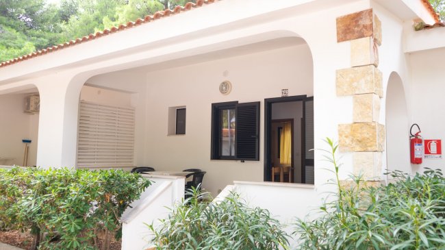 Veranda di una casa bianca con piante e sedie.