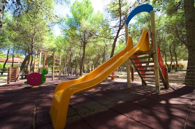 Scivolo giallo in un parco giochi tra alberi alti.