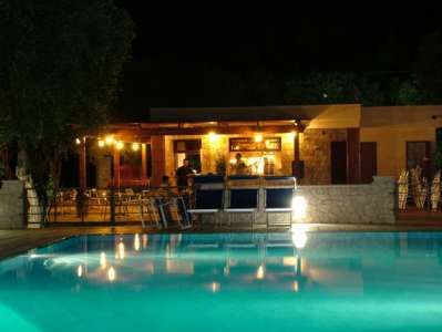Piscina illuminata di notte, con un bar in pietra sullo sfondo.