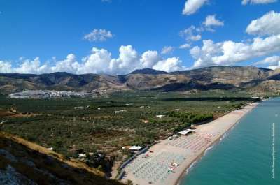 Una lunga spiaggia sabbiosa con ombrelloni, vista panoramica di colline e cielo blu.