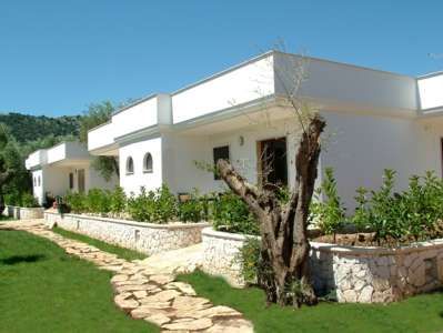 Bungalow bianchi con un giardino verde e un sentiero di pietra di giorno.