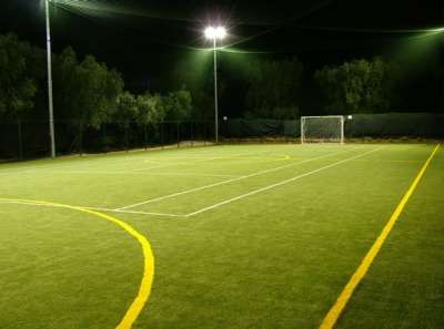 Campo da calcio illuminato di notte con alberi sullo sfondo.