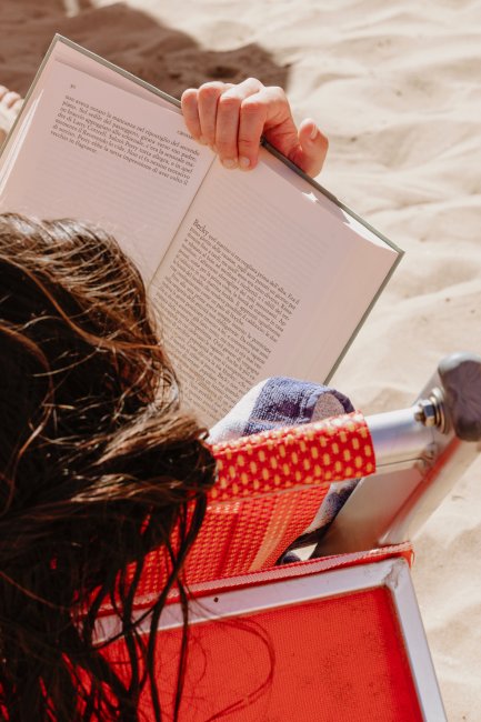 Persona legge un libro su sedia a sdraio in spiaggia.