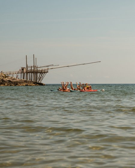Persone su una tavola in mare, vicino a una struttura di legno.