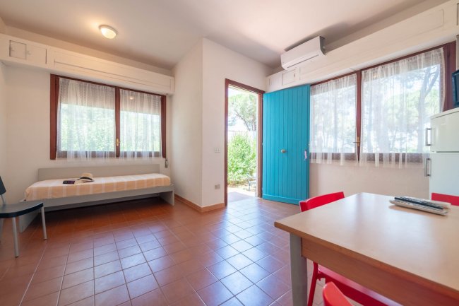 Stanza luminosa con divano, tavolo e porta blu aperta.