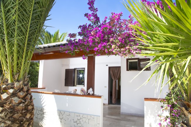 Bungalow bianco con bouganville fiorita e palme.