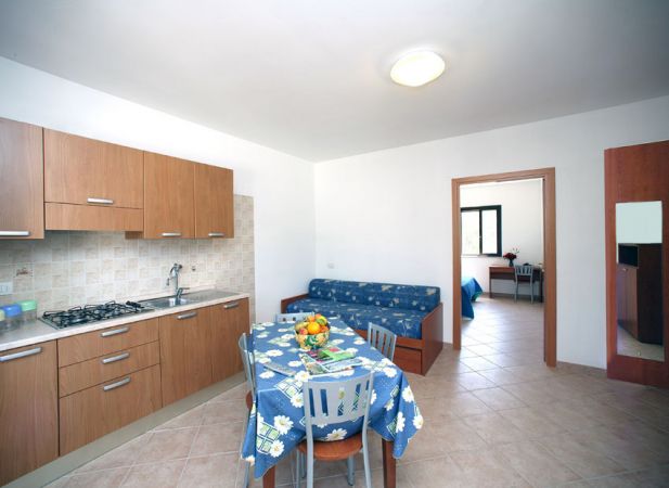 Cucina moderna con tavolo coperto da tovaglia blu a fiori, divano e stanza in secondo piano.