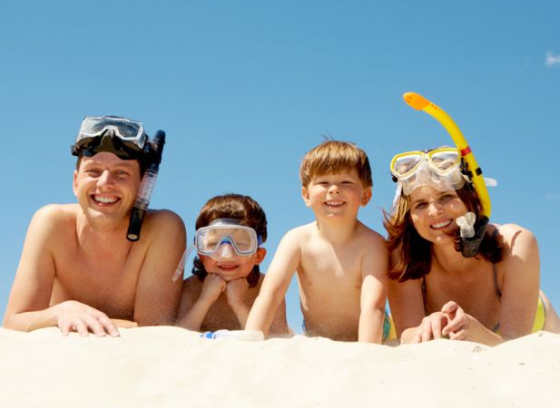 Una famiglia sorridente con maschere da snorkeling sdraiata sulla sabbia.