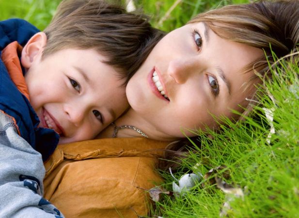 Una madre e un bambino sdraiati sull'erba, entrambi sorridenti.