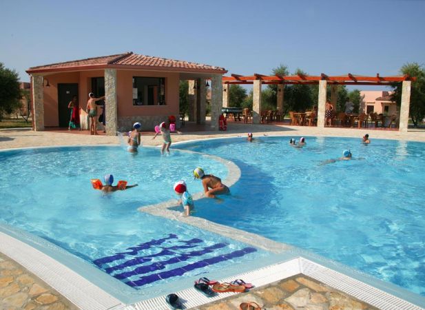 Bambini che nuotano in una piscina all'aperto con un piccolo edificio sullo sfondo.