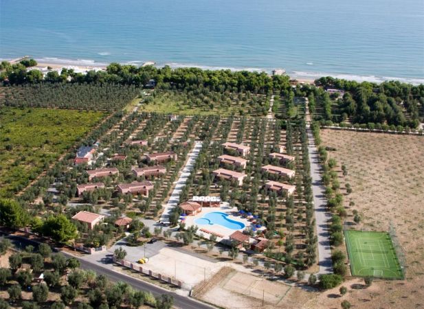Complesso residenziale con piscina, circondato da ulivi e campi coltivati vicino al mare.