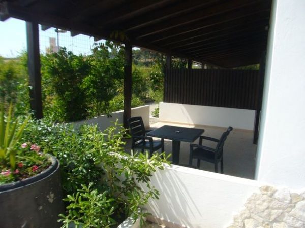 Un patio coperto con tavolo e sedie nere, circondato da vegetazione verde.