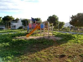 Un parco giochi con uno scivolo arancione su un prato. Sullo sfondo si vedono alberi e una casa.