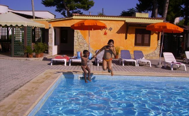 Una donna e un bambino saltano in una piscina vicino a ombrelloni arancioni.