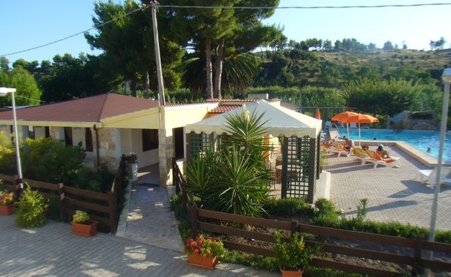 Piscina all'aperto con lettini e ombrelloni accanto a un edificio con giardino.