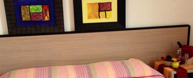 Interno di una camera con un letto a righe colorate e quadri astratti sul muro.