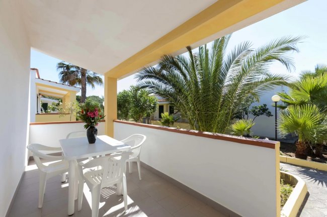 Terrazzino con tavolo bianco e piante tropicali.