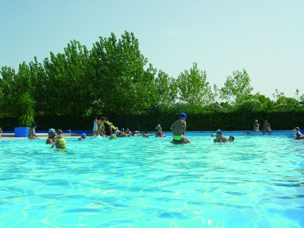 Una piscina affollata con persone che nuotano e alberi sullo sfondo.