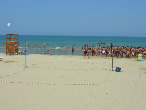 Una spiaggia con campo da pallavolo e persone che si radunano vicino all'acqua.