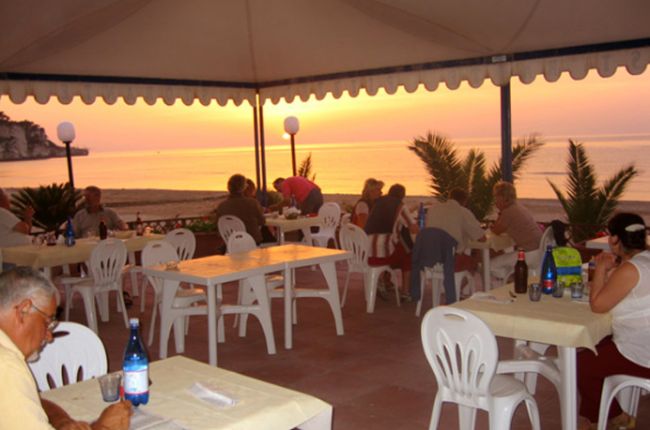Persone cenano sotto un tendone al tramonto.