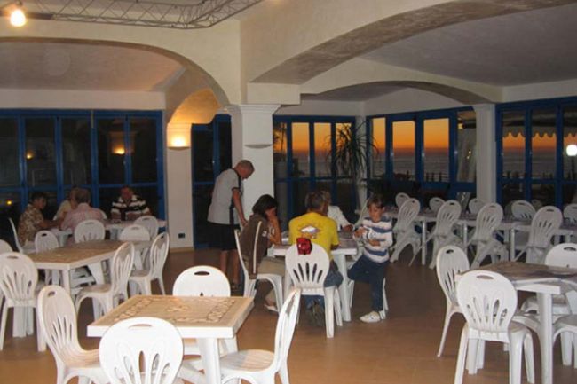 Sala con tavoli e sedie bianche, vista mare al tramonto.